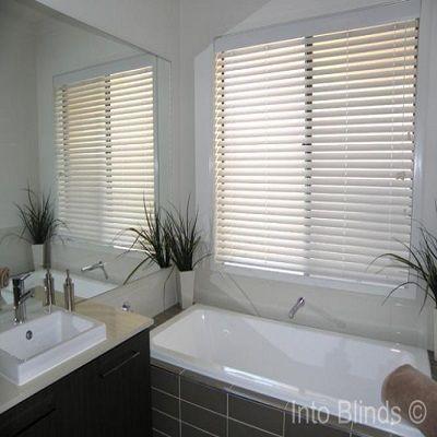 White Venetian Blinds on large window in closed position above bath tub in white colour with dark grey tiled floor.